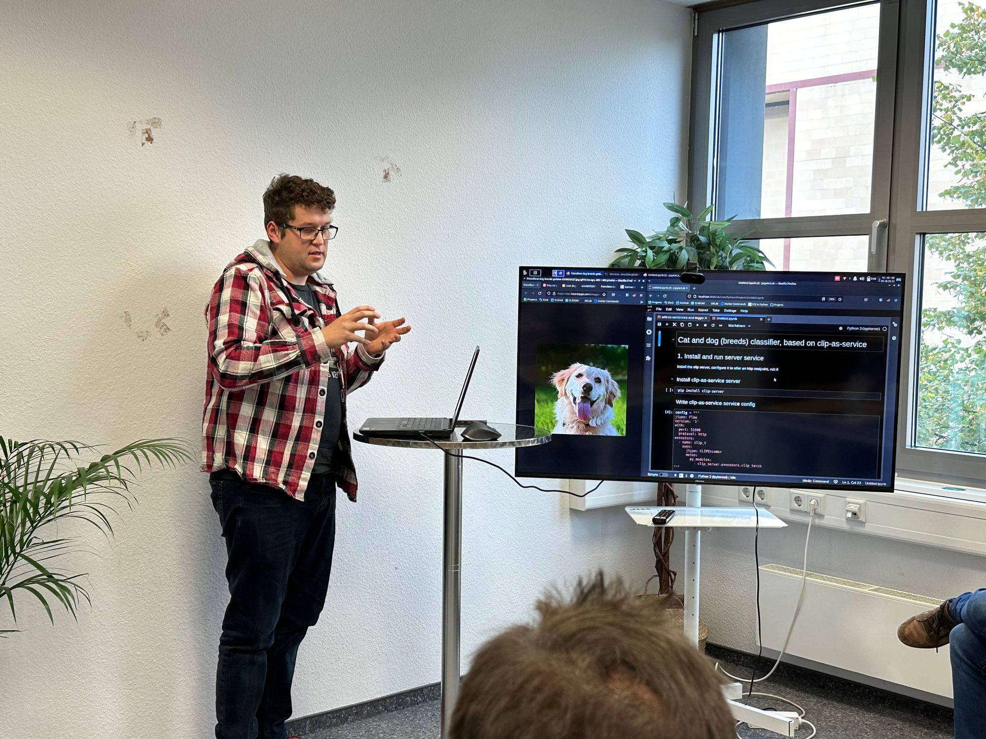 Man in glasses and checkered shirt presenting a cat and dog breeds classifier, with a related code visible on the TV screen