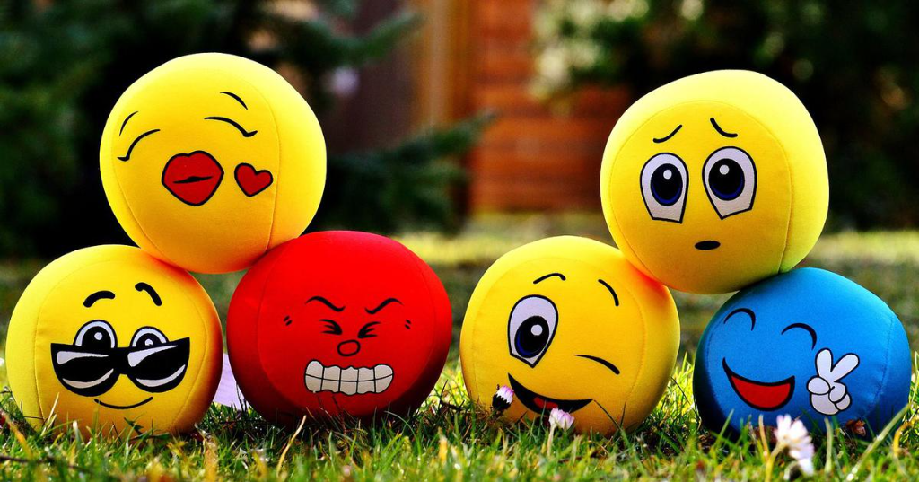 Six emoji stress balls with assorted expressions arranged on a grassy field, evoking a playful atmosphere