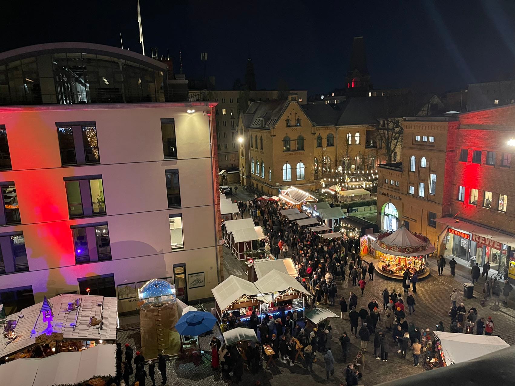 Festive Christmas market at night with bustling crowds, illuminated stands, and historic buildings adorned with lights