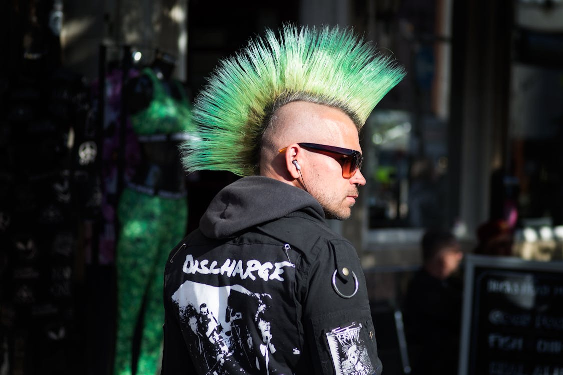 Man with a green mohawk and black "DISCHARGE" coat on a city street, showcasing bold fashion and individuality.