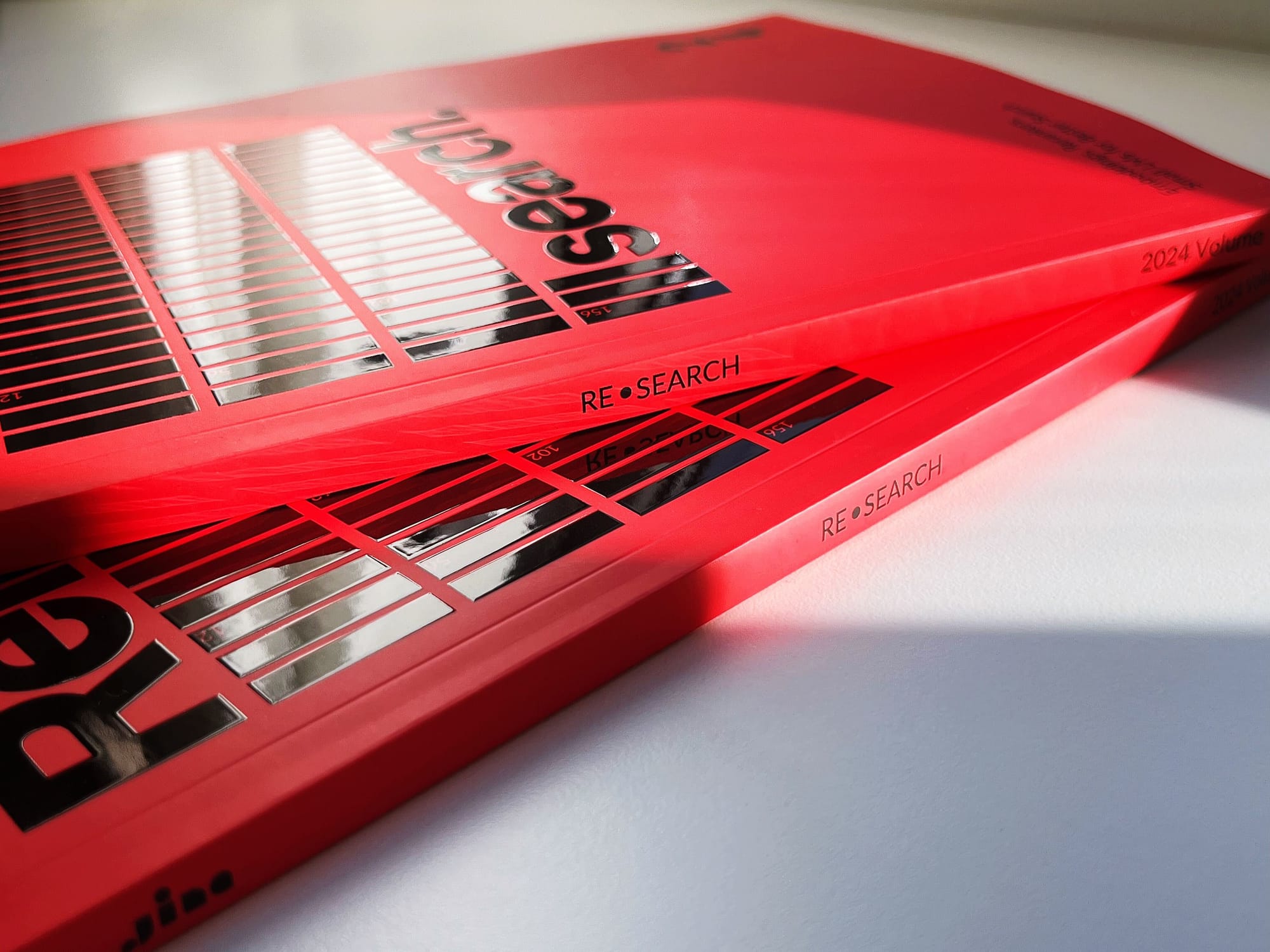 Two red books titled "RESEARCH" stacked on a white background, with "2024 Volume" visible, creating a minimalist aesthetic.