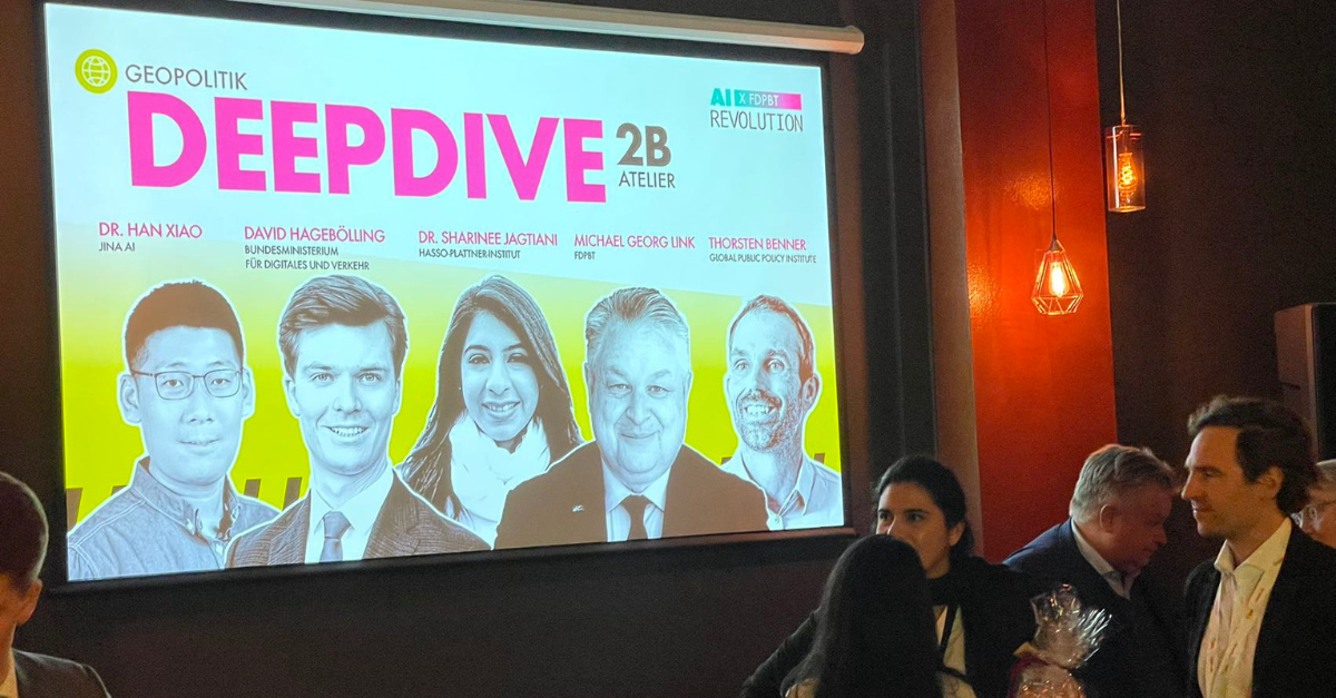 Conference attendees engage in discussion in front of a presentation screen displaying "DeepDive 2B" with names and affiliati