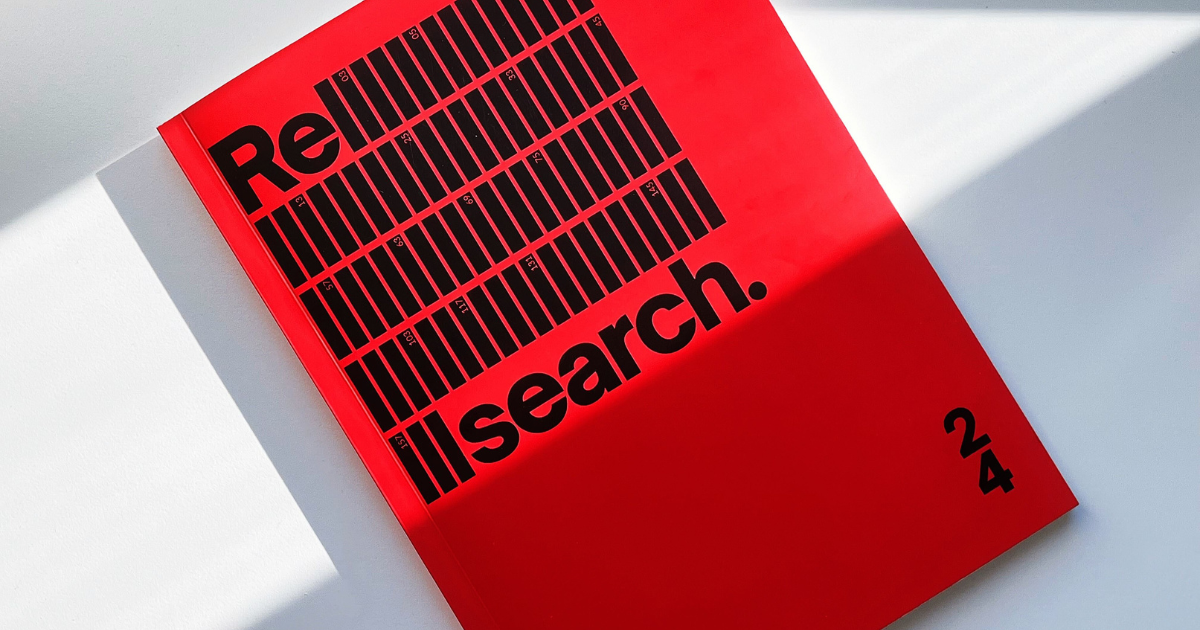 Open red publication "ReSearch" volume 24 displayed on a white surface with a distinctive shadow casting over the pages.